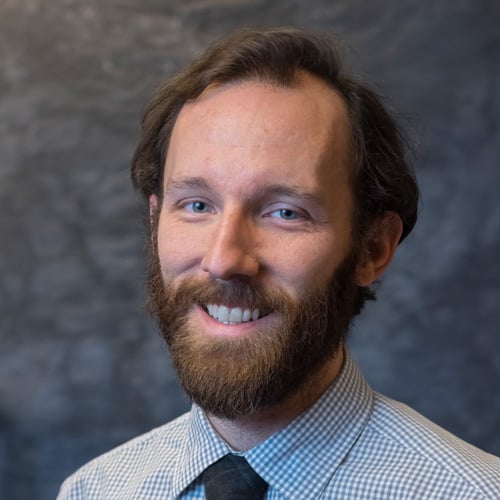 Scott smiling with beard in professional headshot against gray mottled background