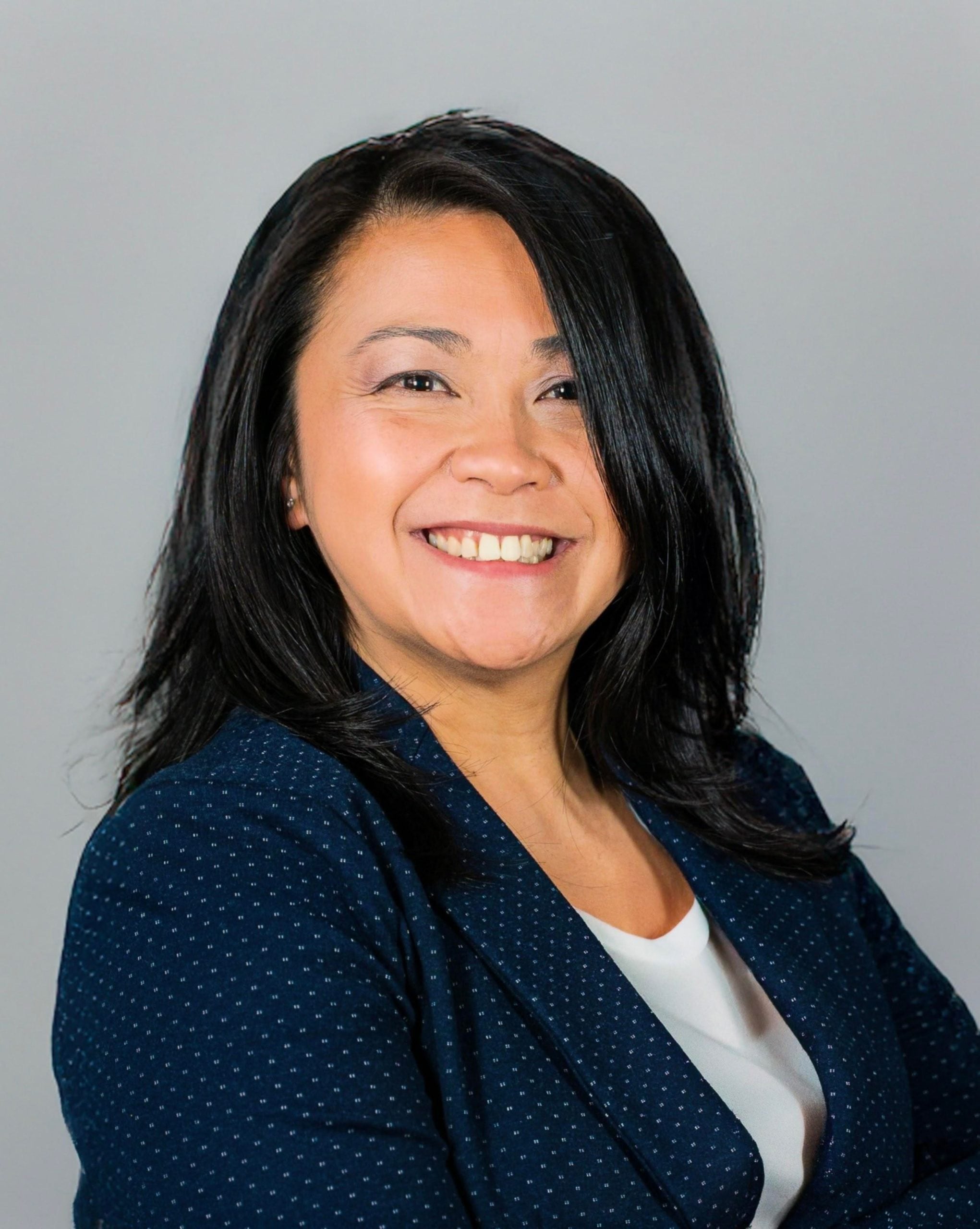 Abby smiling in blue blazer against light gray background