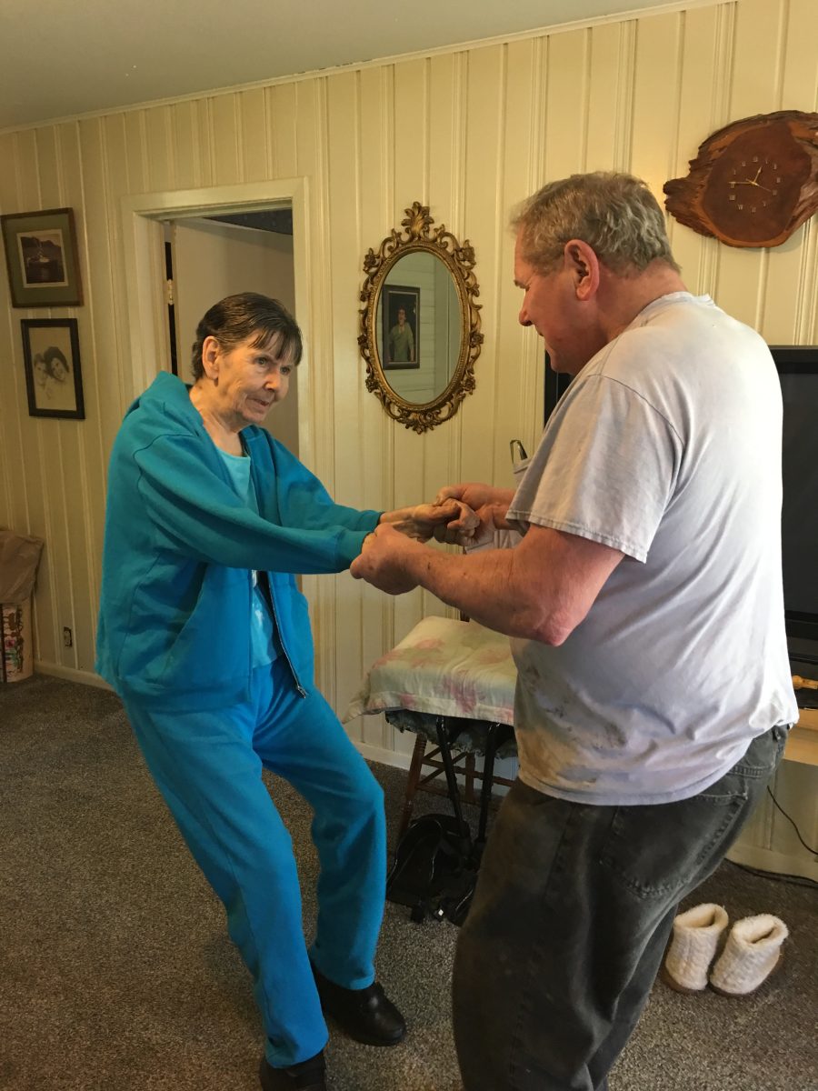 Charles and Irene hold hands dancing in home foyer