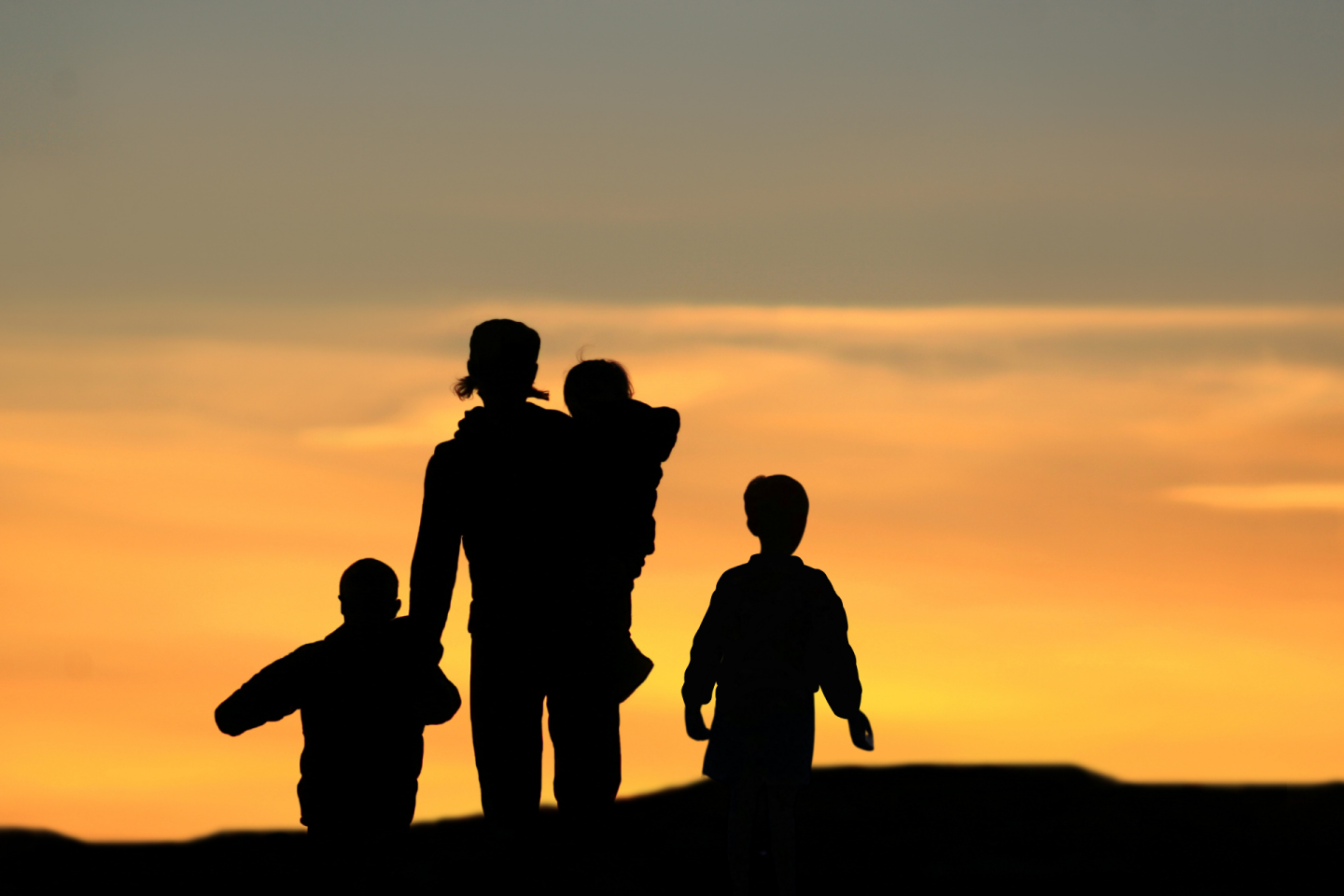 Silhouette of adult with three children before a beautiful sunrise