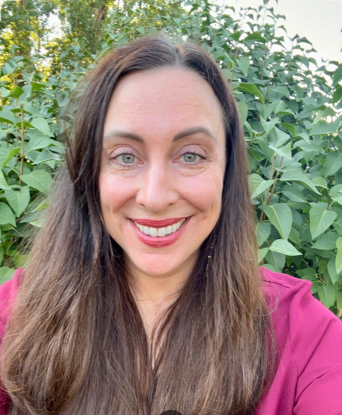 Nicole smiling outdoors in front of verdant bush
