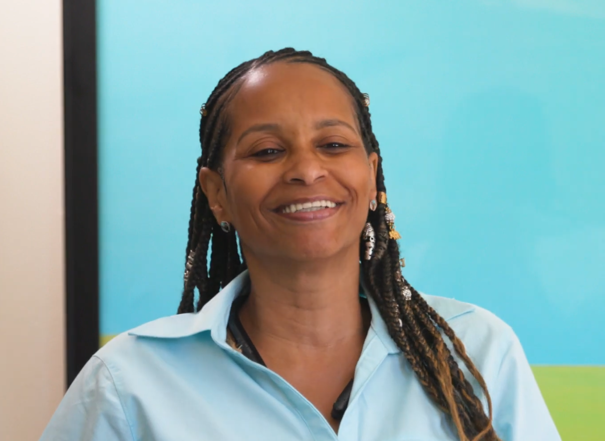 Anita with a large grin in front of bright blue and green poster