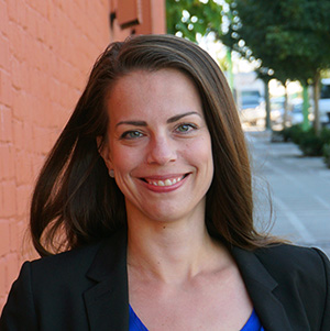 Laura smiling on city sidewalk against brick red wall