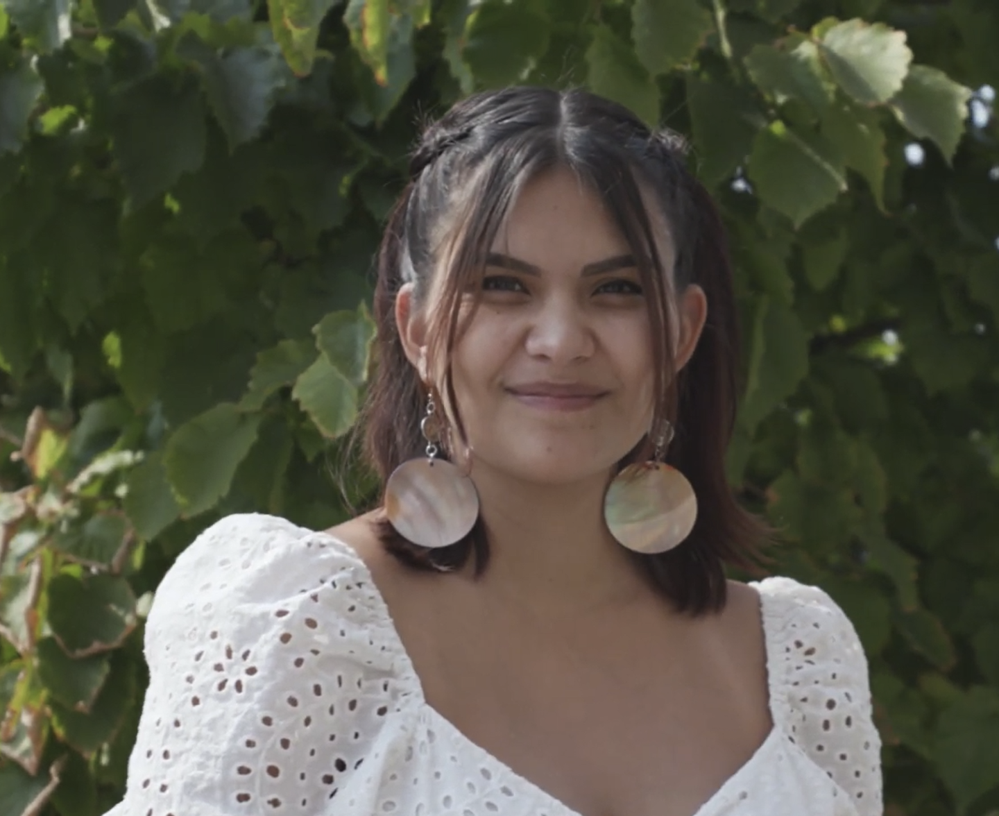Kalaya stands smiling before wall of green vines