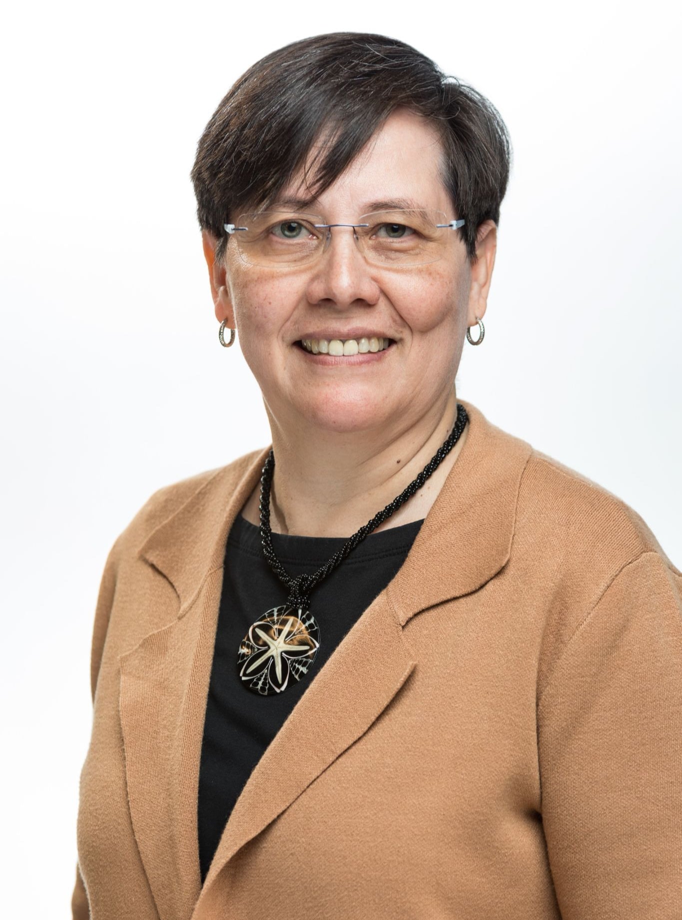 Alma smiling in tan blazer against white background