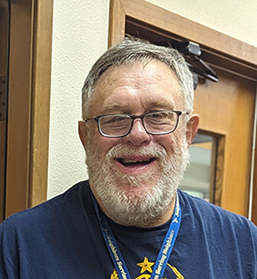 Richard smiling with glasses and lanyard around neck in office office hallway