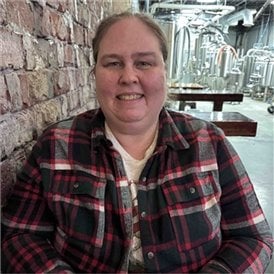 Luanne in plaid shirt smiling and leaning on old brick wall