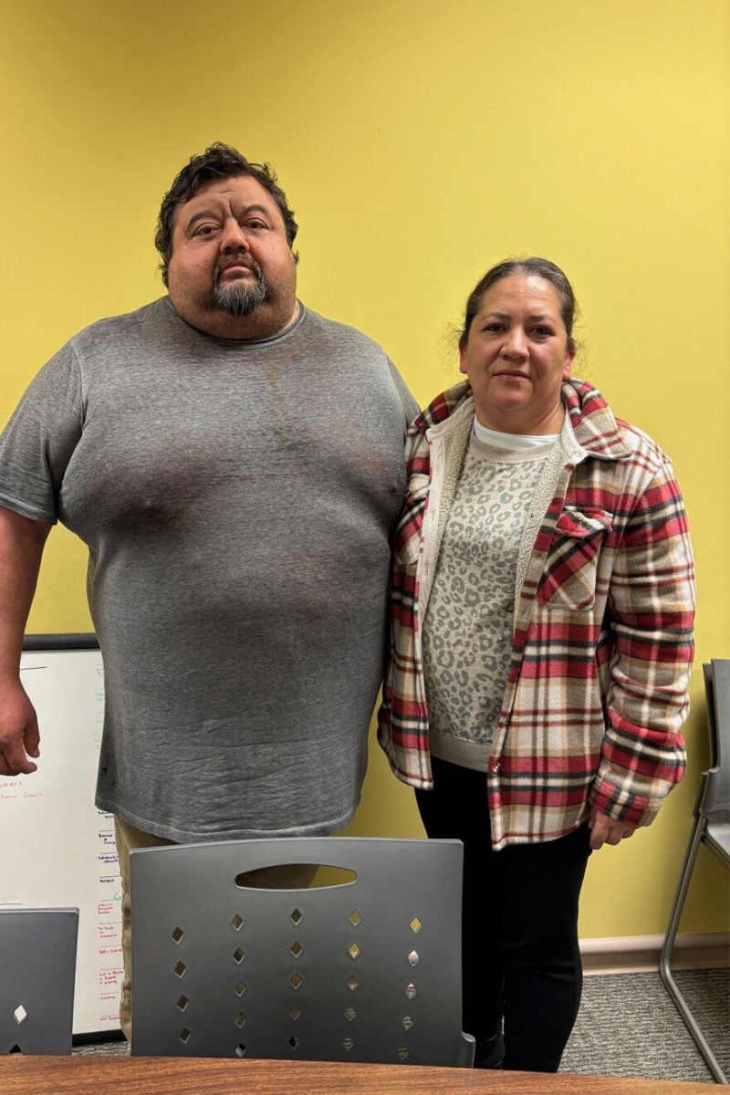 Maria and her husband stand before a lemon-yellow wall