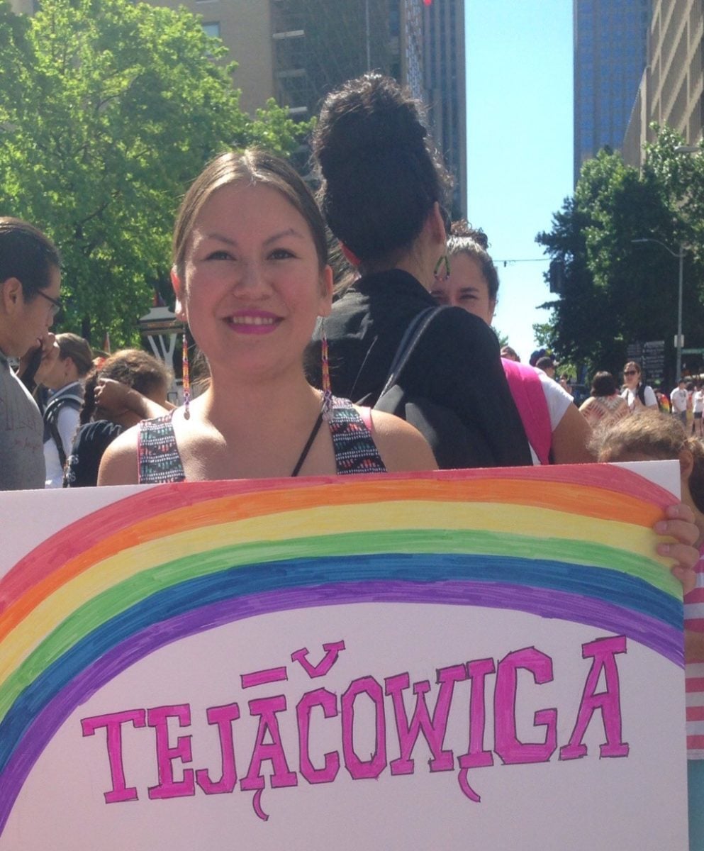 Smiling woman holds hand-drawn poster with rainbow over work TEJACOWIGA