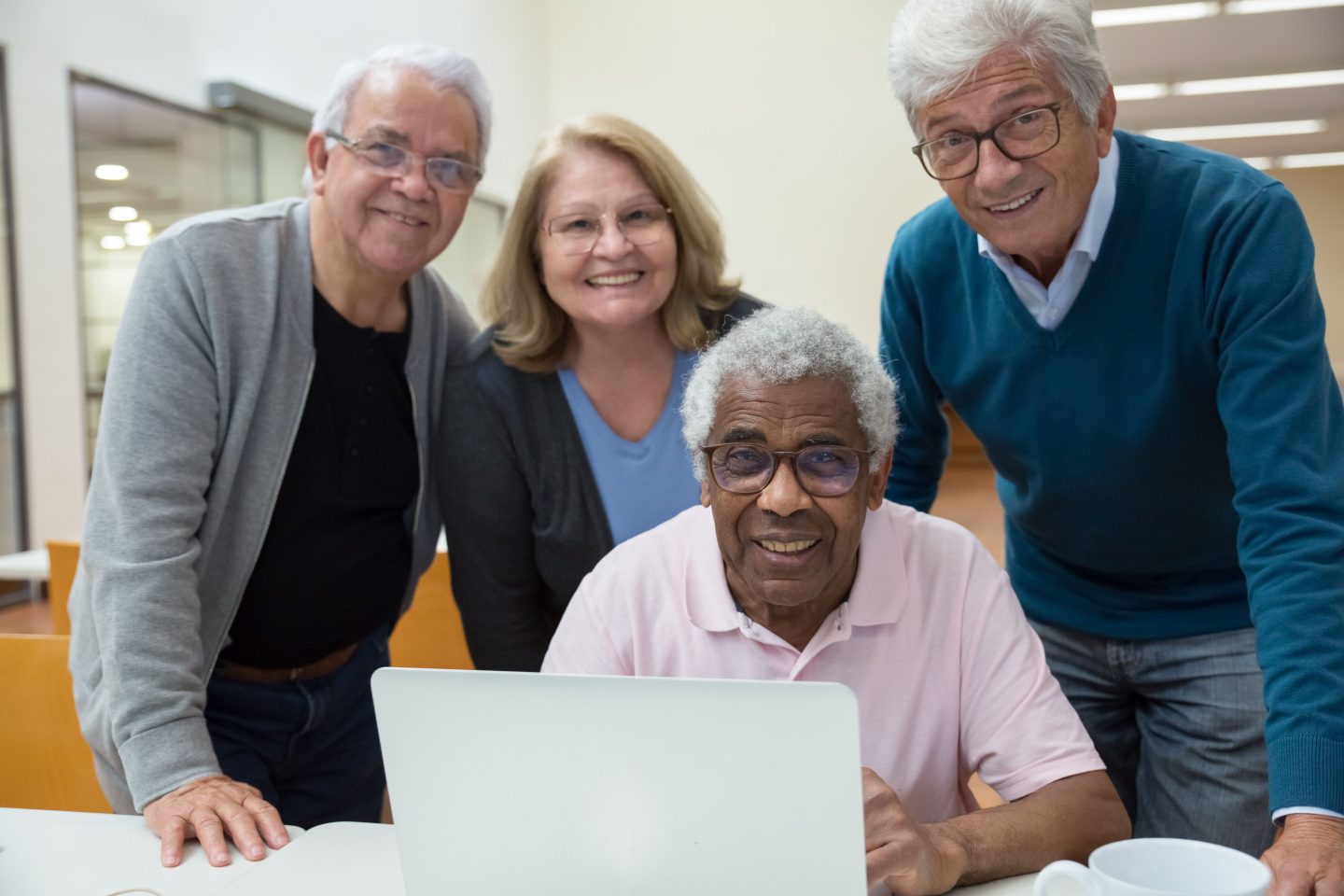 Group of four seniors smiling for the camera around a laptop